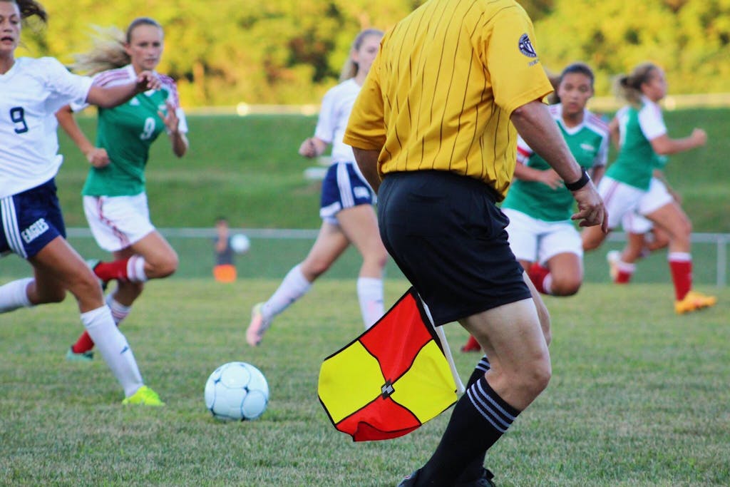 Women's soccer match featuring players and referee on field in motion.